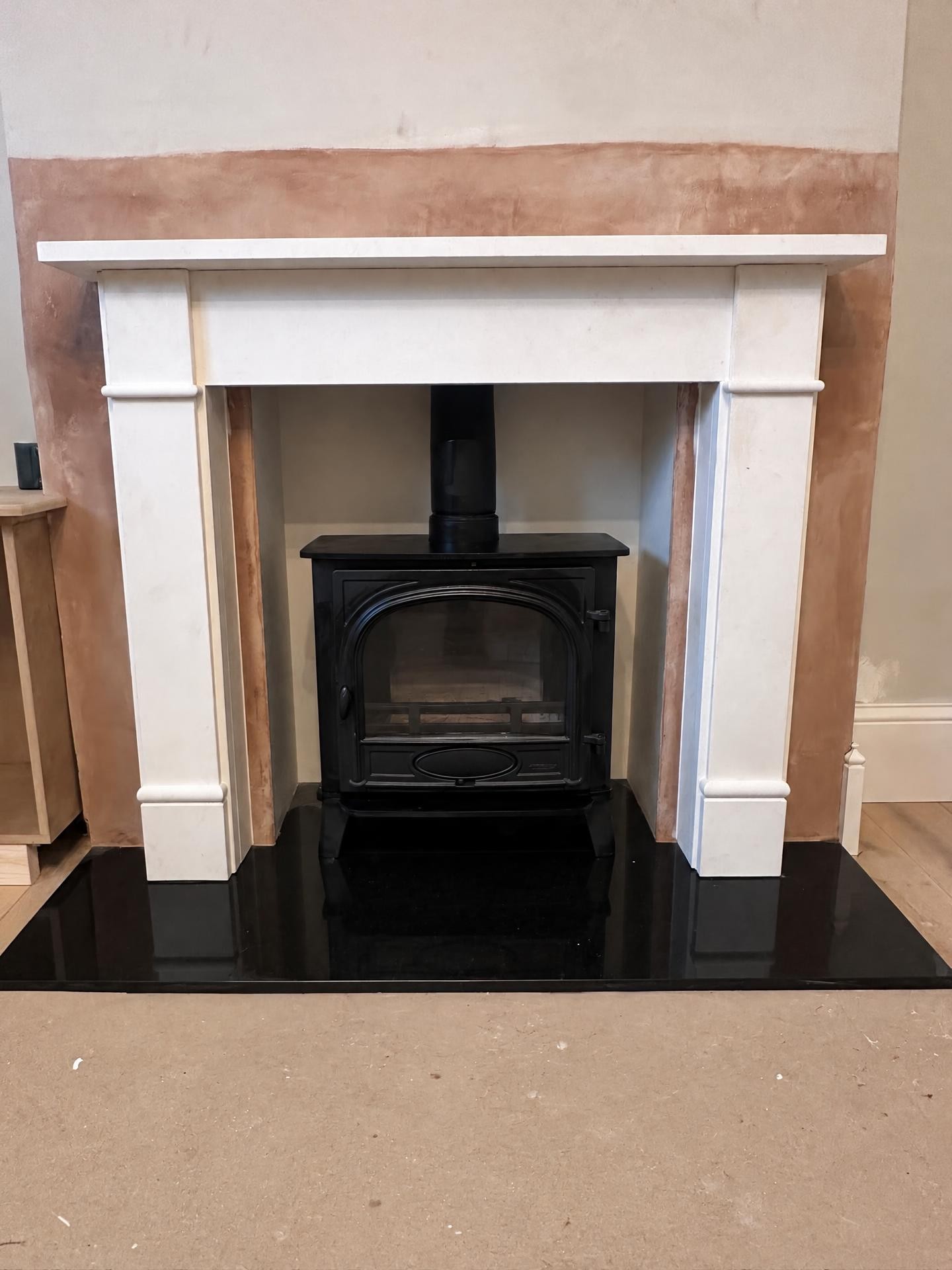 White fireplace surround with a new cast-iron stove while the walls are still being plastered