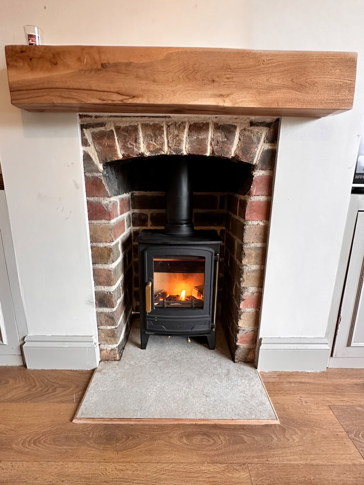 Lit wood burner in a rustic brick fireplace with a curved arch and an oak mantel