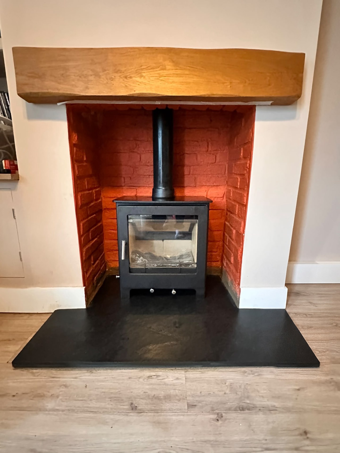 Freestanding black stove in a red brick inglenook with an oak beam and slate hearth