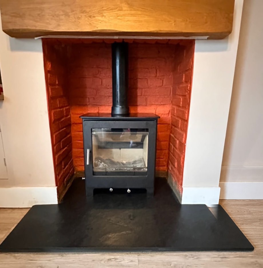 Freestanding black stove on a slate hearth inside a red brick recess
