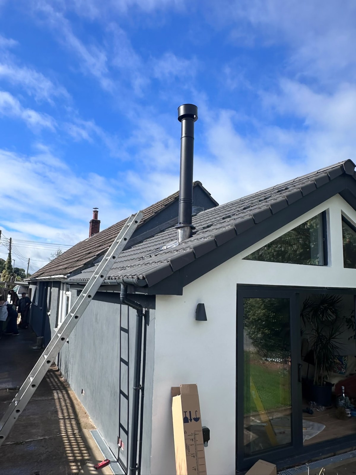 Black twin-wall flue rising through a tiled roof on a garden-room extension