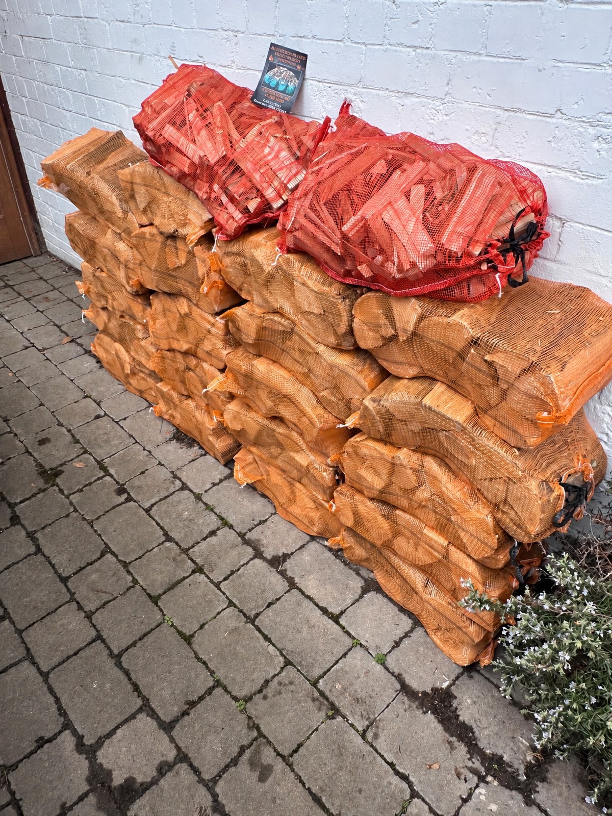 Netted sacks of logs and kindling stacked against an exterior wall, ready to burn