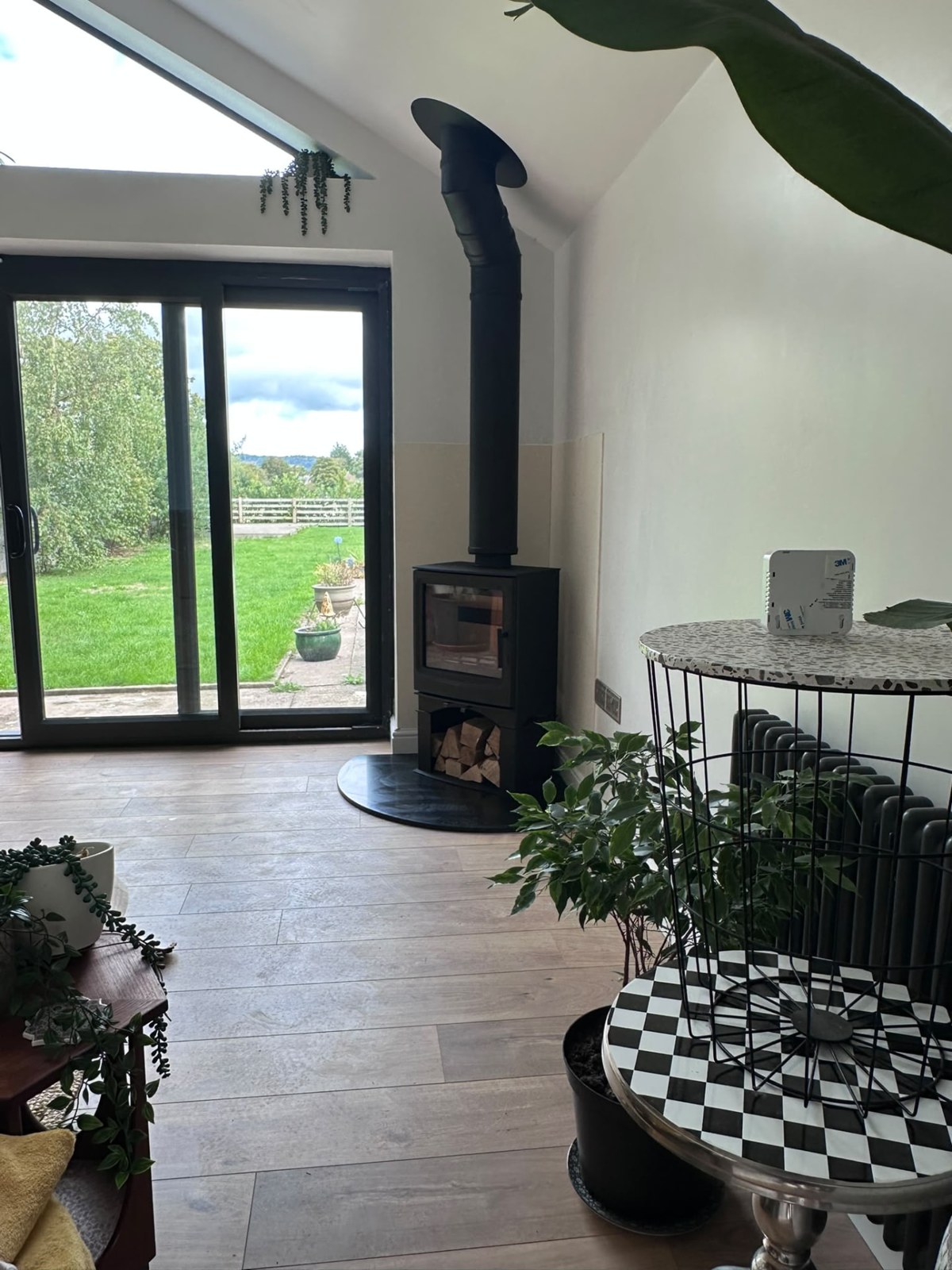 Black wood burner on a curved slate hearth in a bright garden room with a twin-wall flue