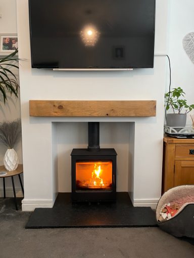 Modern log burner in a white fireplace with oak mantel and lit fire