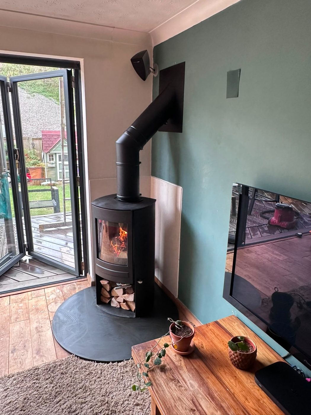 Black wood burner on a round hearth by folding garden doors