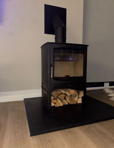 Freestanding black wood burner with built-in log store on a granite hearth