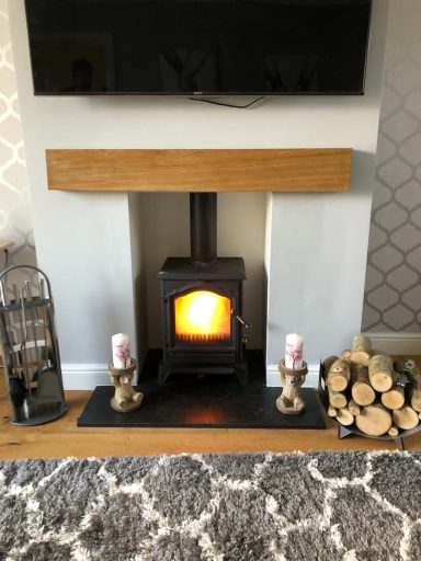 Wood burner under a rustic oak beam in a brick fireplace, burning bright