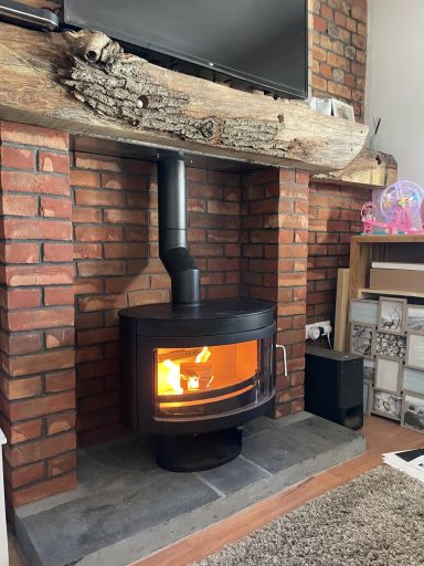 Exposed brick chimney breast with a lit wood burner and log baskets